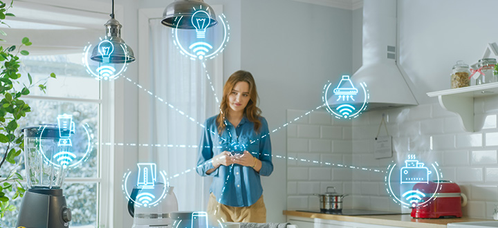 A lady standing in the kitchen and operating her mobile phone. An representation of Smart home automation.